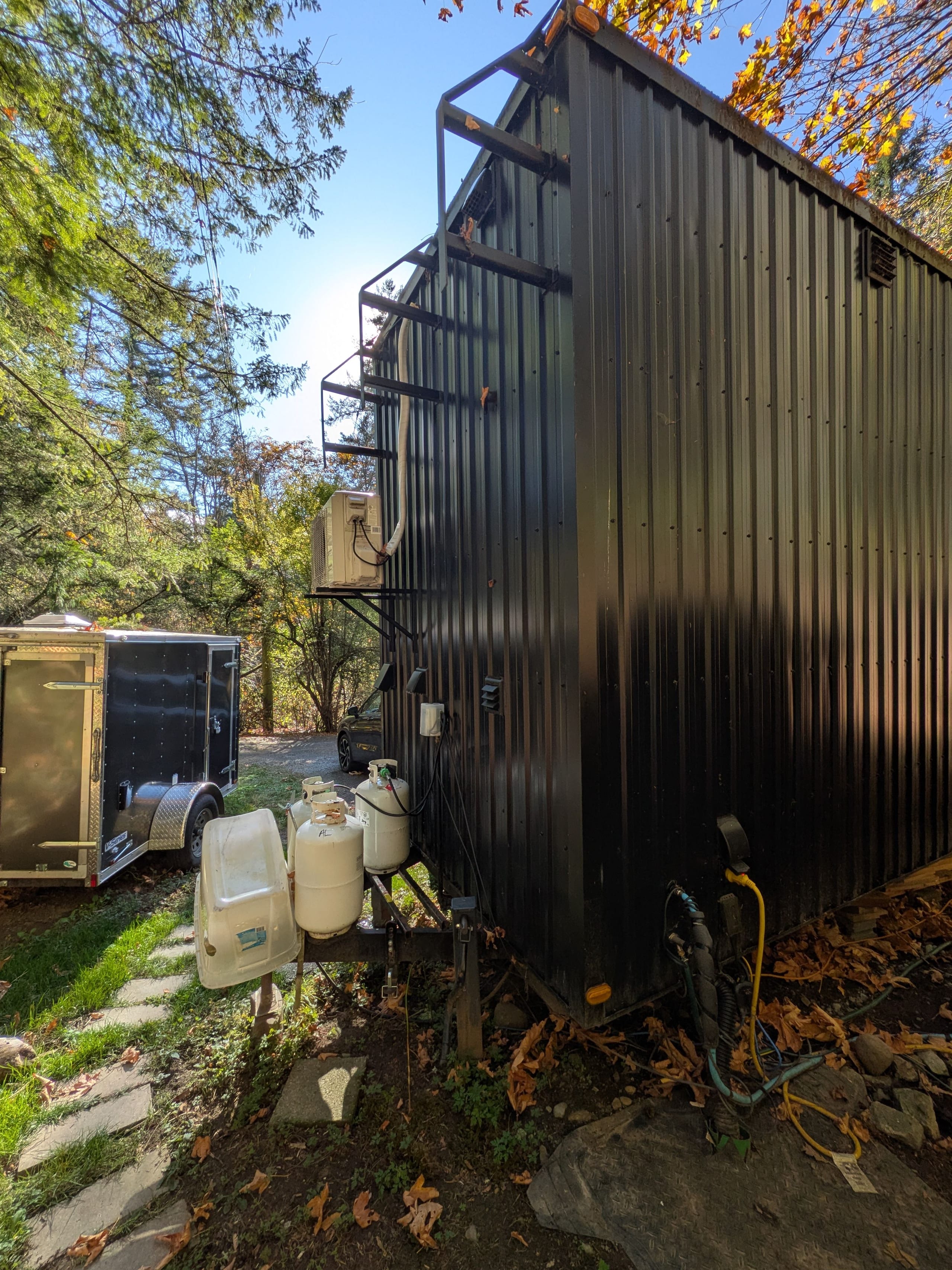 Dark steel siding and rear corner of the tiny house beside a storage shed