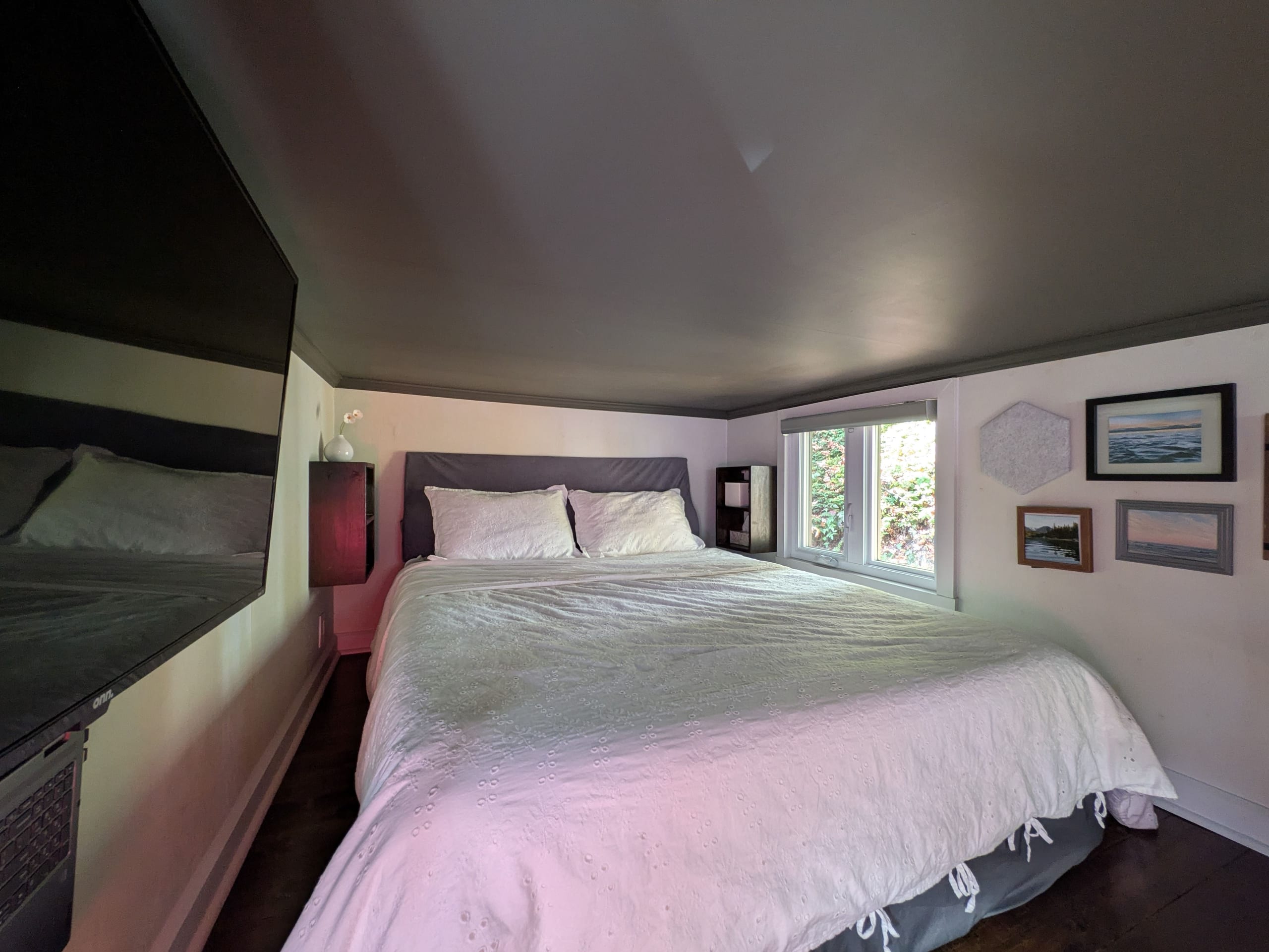 Sleeping loft with bed, window and framed artwork